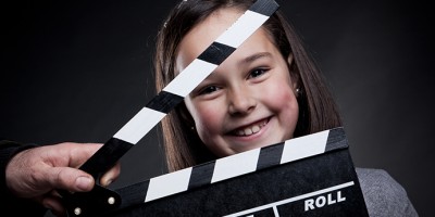 Portrait of smiling young girl behind a movie clapper board