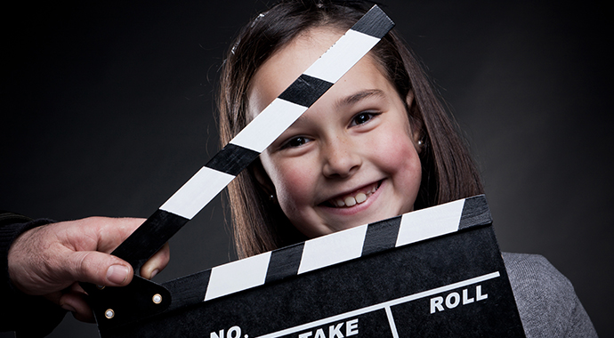 Portrait of smiling young girl behind a movie clapper board